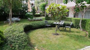 Een verzorgde tuin met een kleine boom, strakke hagen en terrasmeubilair.