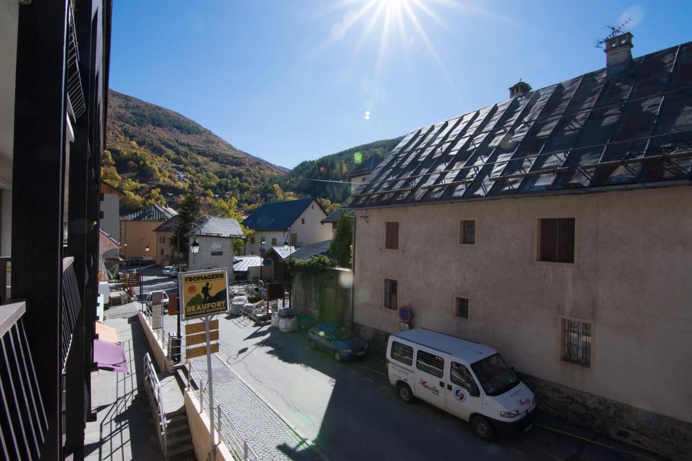 A narrow street with a parked van, buildings with sloped roofs, and a mountainous backdrop.