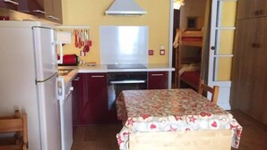 A compact kitchen with a refrigerator, stove, and hanging utensils. A small dining table with a patterned tablecloth is in the center. - 10m from ski slopes, 2nd floor, view ski slopes, balcony, tv, ski locker, 30m², Risoul (Risoul)