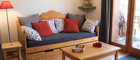 A cozy room with a wooden sofa, a small wooden table, a lamp, and a clock on the wall.