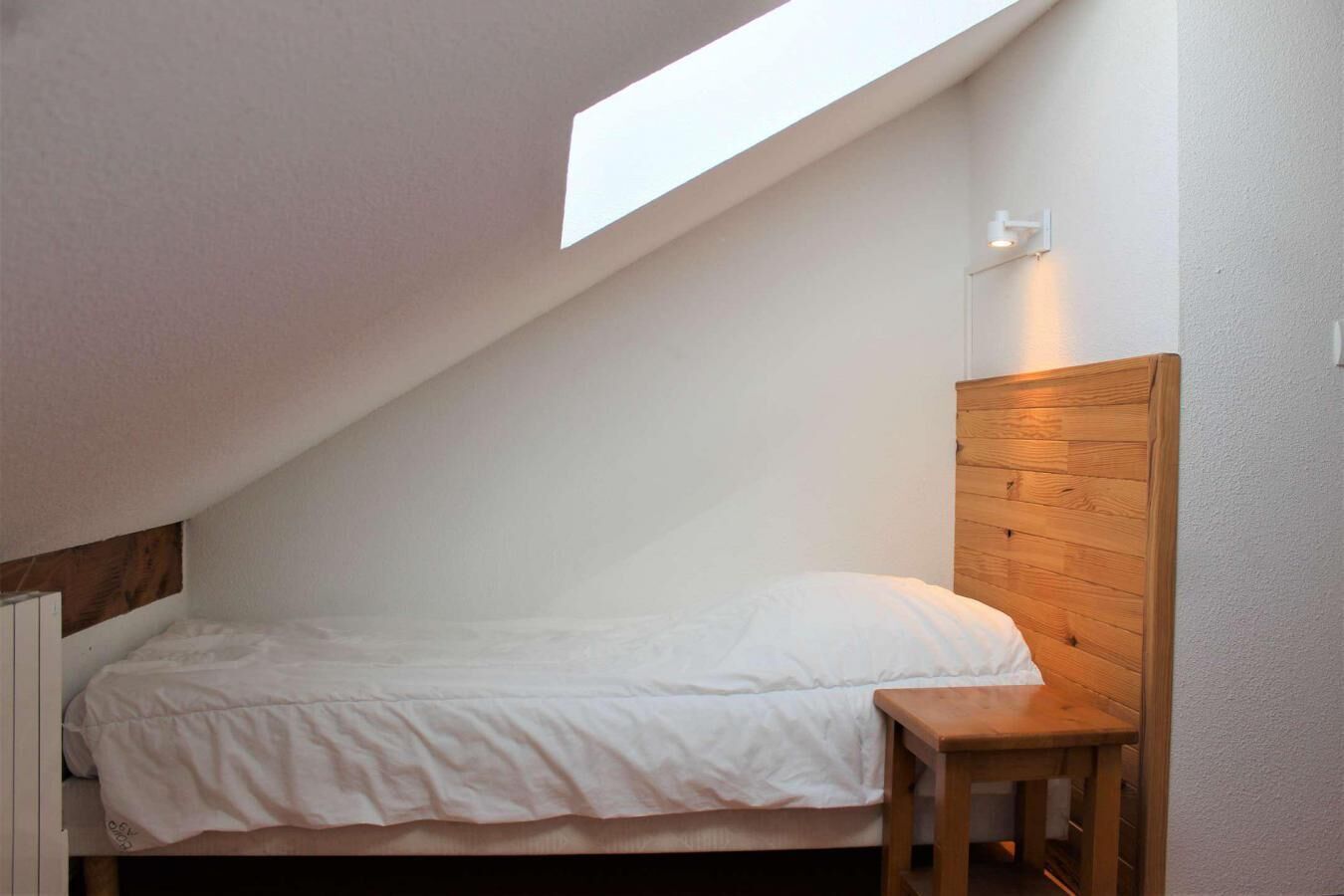 A small, single-bed room with a sloped ceiling and a skylight.