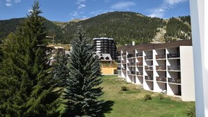 A hotel with a modern design, featuring a multi-story structure with balconies. The building is surrounded by a well-maintained lawn and tall evergreen trees. - 50m from ski slopes, 3rd floor, view village/ski slopes, balcony, parking, tv, ski locker, 42m² (Montgenèvre)