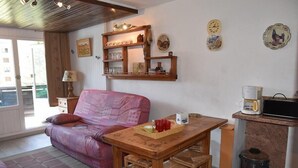 A cozy living room with a pink sofa, wooden dining table, and chairs. There is a kitchen area with a coffee maker and a trash can. - 50m from ski slopes, 3rd floor, view village/ski slopes, balcony, parking, tv, ski locker, 42m² (Montgenèvre)