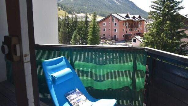 A balcony with a blue chair, a view of a mountain, and a building with red walls. - 50m from ski slopes, 3rd floor, view village/ski slopes, balcony, parking, tv, ski locker, 42m² (Montgenèvre)