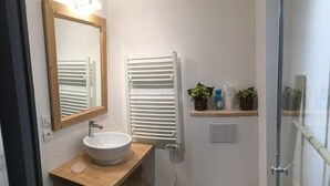 A modern bathroom with a wooden vanity, a white sink, a mirror, a towel rack, a toilet, and a shower area.