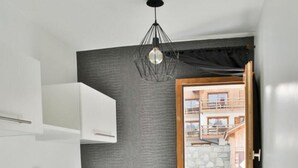 A small, modern room with two single beds, a large window with a view of a building, and a unique pendant light fixture.