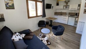 A modern living room with a sofa, two chairs, a small table, and a kitchen area with white cabinets and a microwave.