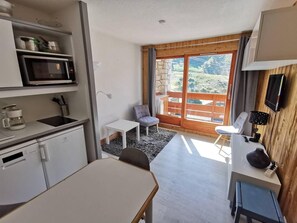 A compact kitchen with a microwave, sink, and cabinets, a dining area with a table and chairs, and a balcony with a view of the outdoors.