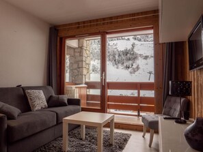 A cozy living room with a sofa, a small table, and a view of a snowy landscape through a glass door.