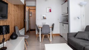 A modern living room with a dining area, a kitchen, and a TV mounted on a wooden wall. - 130m from ski slopes, 8th floor, view mountain, balcony, ski locker, 23m², Méribel-Mottaret (Méribel - Les Allues)