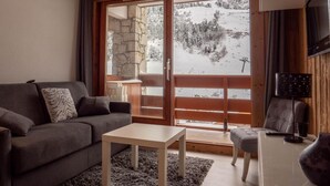 A cozy living room with a sofa, a small table, and a view of a snowy landscape through large glass doors. - 130m from ski slopes, 8th floor, view mountain, balcony, ski locker, 23m², Méribel-Mottaret (Méribel - Les Allues)