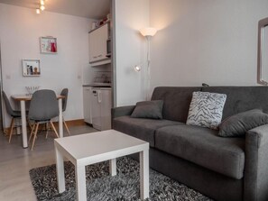 En moderne stue med en grå sofa, et hvidt sofabord og et spiseområde med stole og et lille bord.