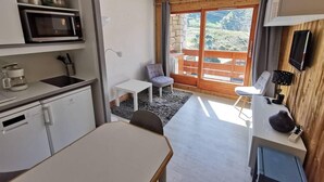 A compact kitchen with a microwave, sink, and cabinets, a dining area with a table and chairs, and a balcony with a view of the outdoors. - 130m from ski slopes, 8th floor, view mountain, balcony, ski locker, 23m², Méribel-Mottaret (Méribel - Les Allues)