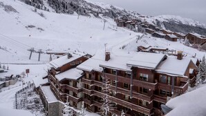 A snow-covered mountain lodge with multiple floors and balconies, surrounded by snowy slopes and a ski lift. - 130m from ski slopes, 8th floor, view mountain, balcony, ski locker, 23m², Méribel-Mottaret (Méribel - Les Allues)
