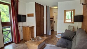 A living room with a sofa, a wooden coffee table, and a television. There is a door leading to a balcony.