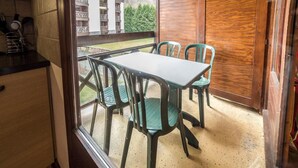 A balcony with a table and chairs, a view of a building, and a wooden door.