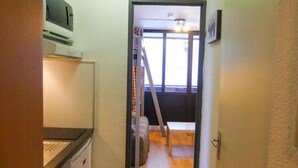 Un couloir étroit, avec un four à micro-ondes posé sur une étagère, une échelle appuyée contre un mur et une porte donnant sur une pièce avec une fenêtre.