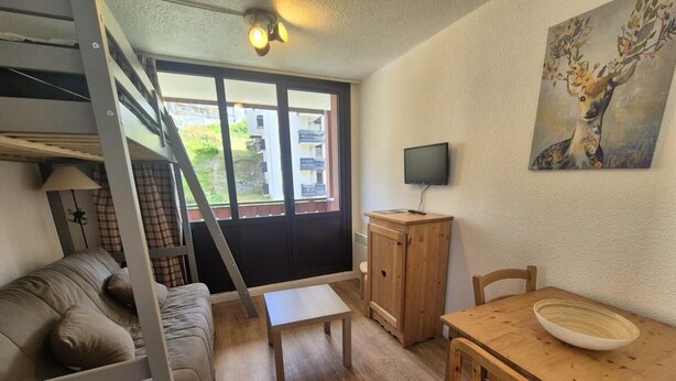 Un espace de vie compact comprenant un lit superposé, une petite table, un meuble en bois et une table à manger avec des chaises.