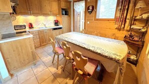 A cozy wooden cabin kitchen with a central island, wooden cabinets, and a dining area with chairs. - Chalet, 160m from resort center, view mountain, terrace, parking, tv, ski locker, 65m² (Saint-Martin-de-Belleville)