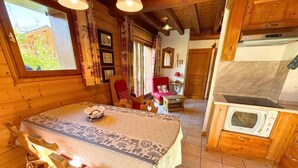 A cozy wooden cabin interior with a dining table, chairs, a red armchair, a small table with a lamp, and a kitchen area with a stove and oven. - Chalet, 160m from resort center, view mountain, terrace, parking, tv, ski locker, 65m² (Saint-Martin-de-Belleville)