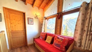 A wooden sofa with red cushions, a wooden door, and a window with curtains. - Chalet, 160m from resort center, view mountain, terrace, parking, tv, ski locker, 65m² (Saint-Martin-de-Belleville)