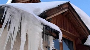 Ein hölzernes Gebäude mit von den Dachvorsprüngen hängenden Eiszapfen und einem Fenster mit Hollerkerung.