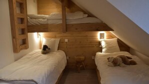 Ein gemütliches Schlafzimmer im Dachgeschoss mit zwei Etagenbetten, einem kleinen Holzschemel und einem Teddybären.