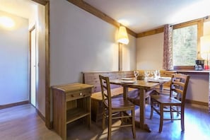 A dining area with a wooden table and chairs, a bench, and a window with curtains.