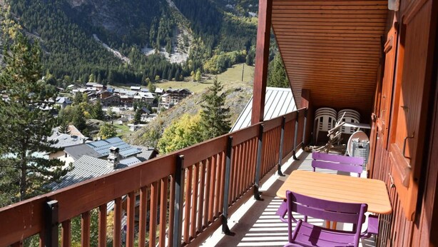 A balcony with a wooden railing, a table, and purple chairs. - 100m from ski slopes, 3rd floor, balcony, fireplace or stove, tv, 75m², Pralognan-la-Vanoise (Pralognan-la-Vanoise)