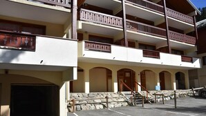 A multi-story building with balconies, a parking area, and a stone wall. - 100m from ski slopes, 3rd floor, balcony, fireplace or stove, tv, 75m², Pralognan-la-Vanoise (Pralognan-la-Vanoise)