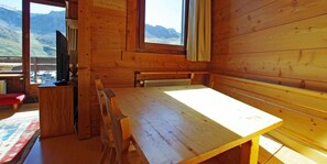 A wooden cabin with a dining table and benches, a television, and a view of mountains through large windows. - 10m from resort center, 10th floor, balcony, tv, 70m², Tignes (Tignes)