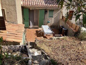 A patio area with a table and chairs, a trash bin, and a covered seating area with a green door.