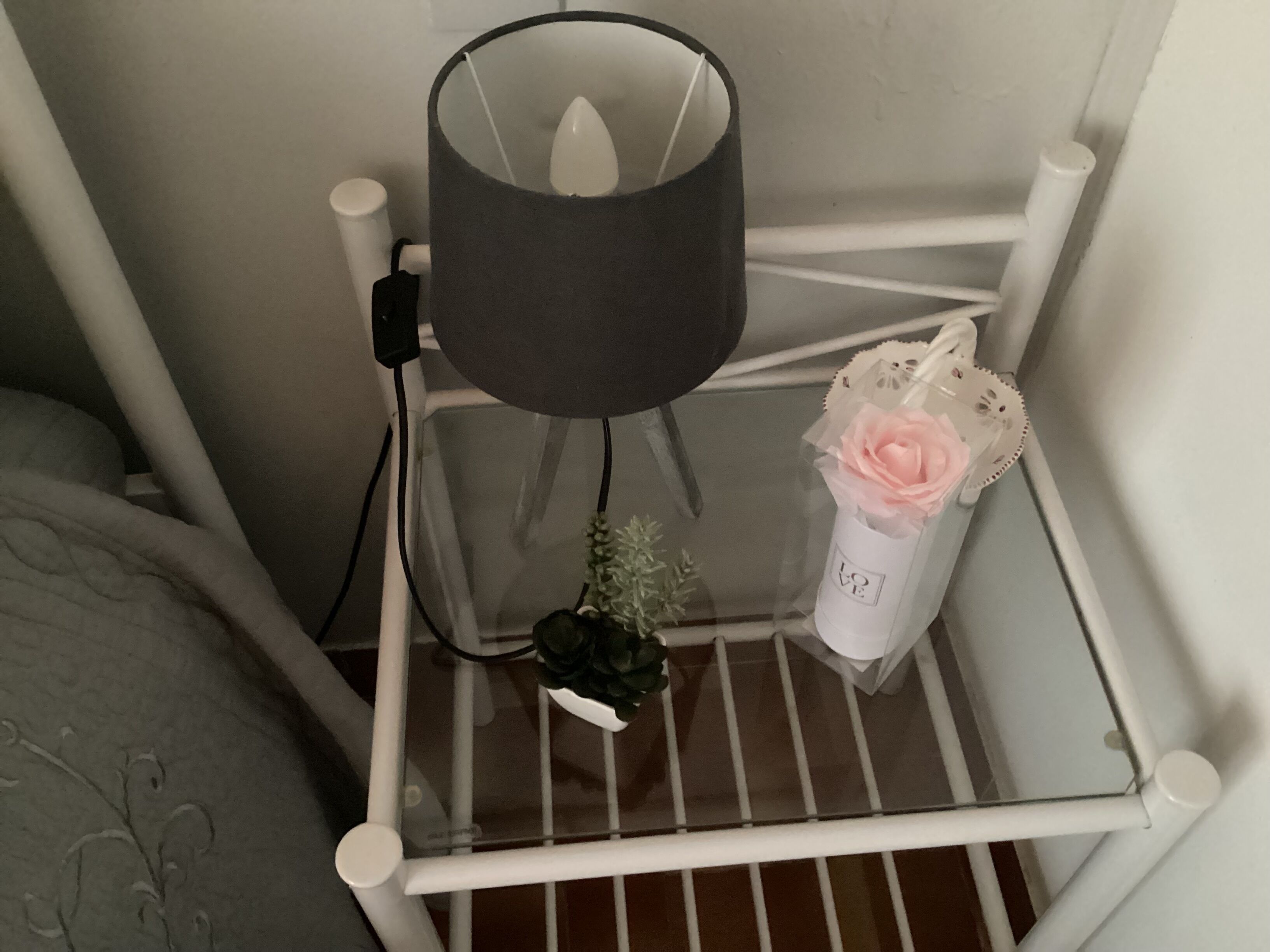 Une étagère en métal blanc, une lampe noire, un vase blanc avec une fleur rose et une petite plante verte.