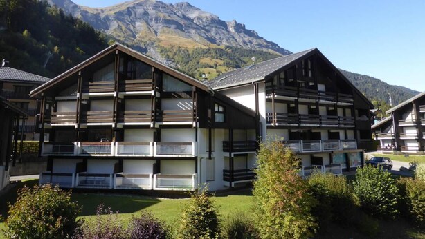 A multi-story chalet with balconies, set against a mountainous backdrop.