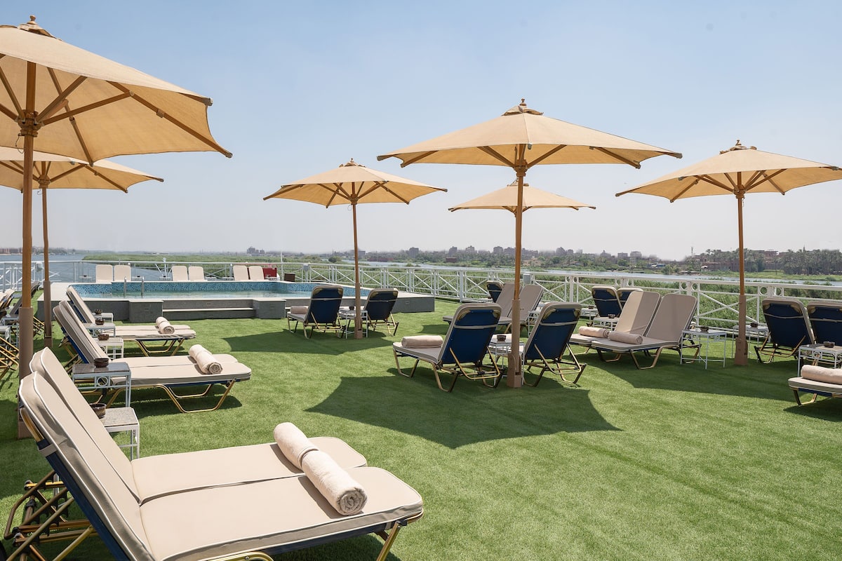 A rooftop lounge area with sun loungers and umbrellas, overlooking a body of water and cityscape.