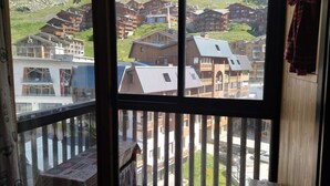 Uma varanda com vista para uma aldeia montanhosa, edifícios de madeira e céu claro.