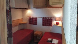 Quarto pequeno e acolhedor com duas camas, armários de madeira e uma mesa.