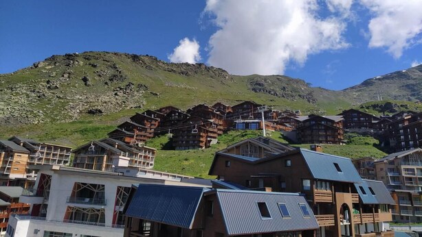 Estância de montanha com edifícios em estilo chalé, teleféricos e um céu azul límpido.