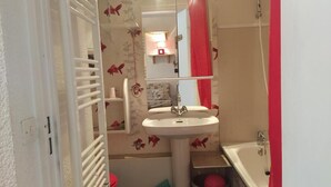 Uma casa de banho com uma pia branca, um espelho, uma cortina de chuveiro vermelha e um porta-toalhas branco.