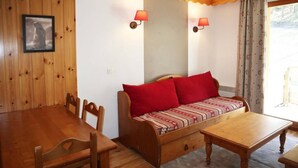A cozy room with a wooden dining table, a sofa with red cushions, and two wall-mounted lamps.