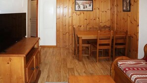 A wooden-paneled room with a TV on a dresser, a dining table with chairs, and a bed with patterned bedding.