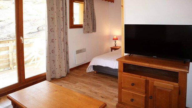 A room with a bed, a television, a wooden table, and a window with curtains.