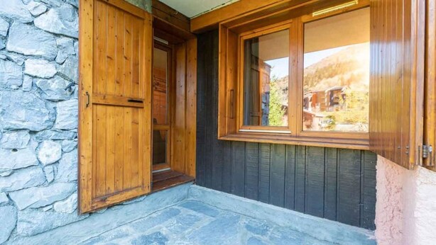 A wooden door with a stone wall and a window with a view of a house.