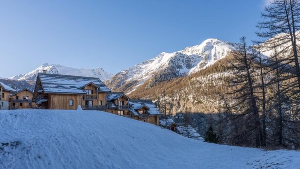Eine schneebedeckte Lodge mit mehreren Holzhäusern vor einer Kulisse schneebedeckter Berge.