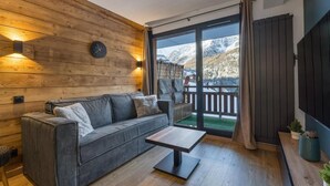 Ein modernes Wohnzimmer mit einer Holzwand, einer Couch, einem Couchtisch und Blick auf Berge durch eine Glastür.