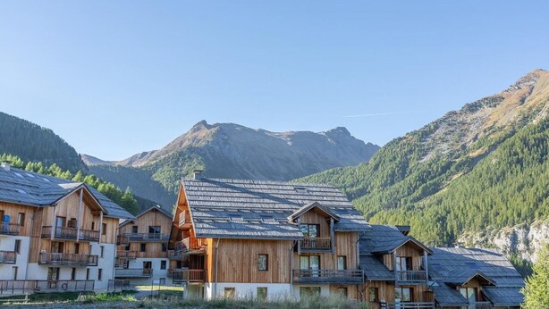 A wooden chalet-style building with multiple balconies and a sloped roof, set against a mountainous backdrop.