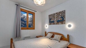 A bedroom with a wooden bed, a window with curtains, a radiator, and a wall-mounted artwork of deer.