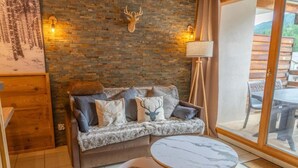 En hyggelig stue med en stenvæg, et dådyrhoved som pynt, en sofa med puder, et rundt bord og en lampe.