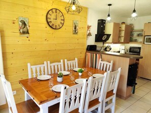 A dining area with a wooden table and white chairs, a kitchen with modern appliances, and a wooden wall with decorative elements.
