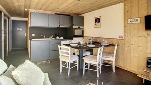Una cocina compacta con armarios grises, una isla central y una zona de comedor con sillas blancas y una mesa oscura.